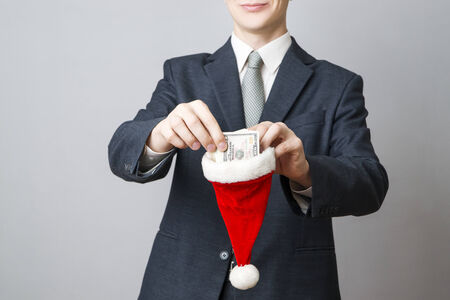 Businessman putting money in a Santa hat on gray backgroundの写真素材