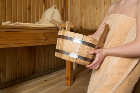 Beautiful woman in sauna, bath accessories. Wooden bucket and sticksの写真素材