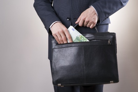 Businessman with a briefcase full of money in the hands of on gray backgroundの写真素材