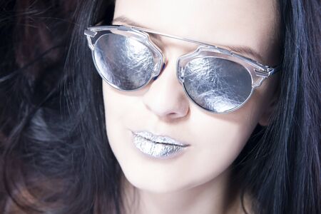 Beautiful woman fashion model portrait in sunglasses with metallic silver lips. Creative hairstyle and make up. Beauty girl close up on a gray backgroundの写真素材