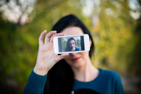 Beautiful young woman doing selfie outdoors. Mobile phone close-up in hand of smiling girl