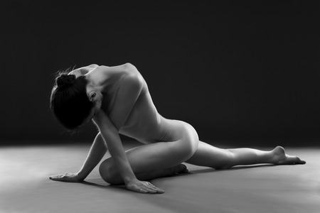 Naked yoga. Beautiful sexy body of young woman on gray background. Low key black and white studio photographyの写真素材