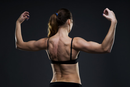 Attractive fitness woman on gray background in studio. Muscular back close-up.の写真素材