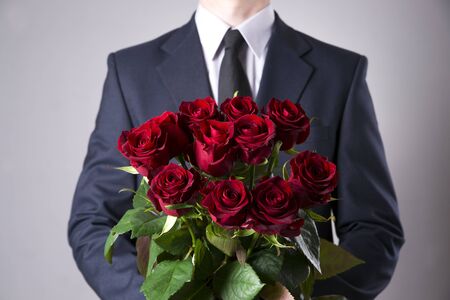 Man with bouquet of red roses on a gray background. Present at the International Women's Dayの写真素材