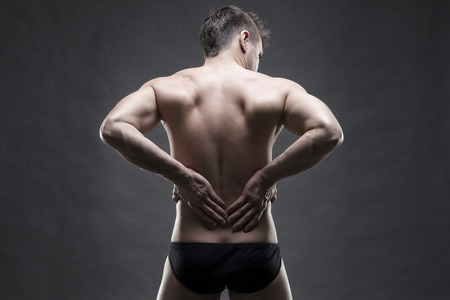 Kidney pain. Man with backache. Handsome muscular bodybuilder posing on gray background. Low key close up studio shot . Sexy male bodyの写真素材