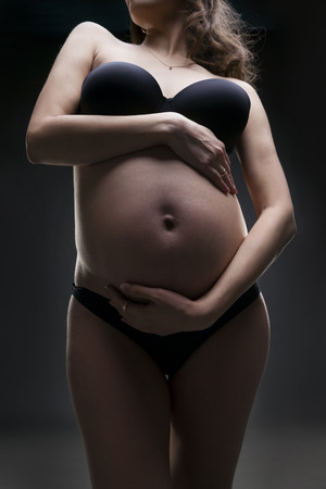 Young beauty and sexy caucasian pregnant woman in black lingerie on gray studio background. Pregnancy conceptの写真素材
