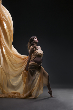 Young beauty and sexy caucasian pregnant woman with yellow silk on gray studio background. Pregnancy concept.の写真素材