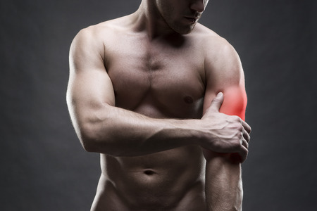 Pain in the elbow. Muscular male body. Handsome bodybuilder posing on gray background with red dotの写真素材