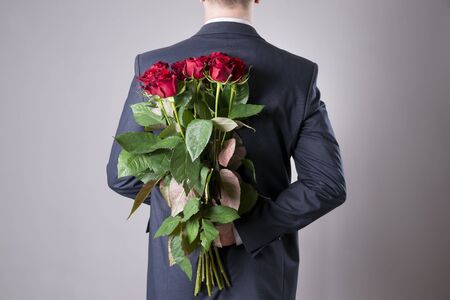 Man with bouquet of red roses on a gray background. Present at the International Women's Dayの写真素材