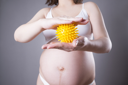 Young caucasian pregnant woman with small yellow massage ball. Close-up studio shot on a gray backgroundの写真素材