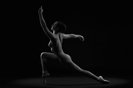 Art nude. Perfect flexible sexy body of young woman on black background. Studio shotの写真素材