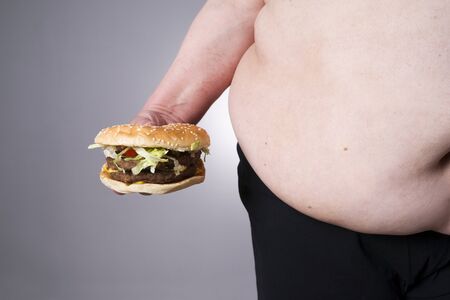 Fat human body with big hamburger in hand. Junk food concept on a gray backgroundの写真素材