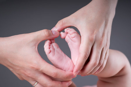 Baby foot in mother's hands on gray background