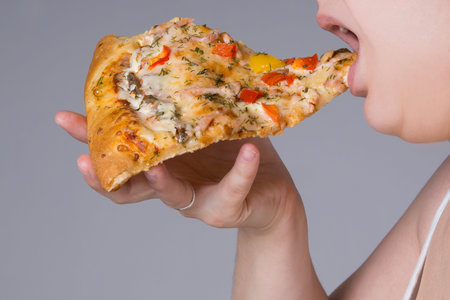 Fat woman with a piece of pizza in hand, closeup on gray background, obesity concept