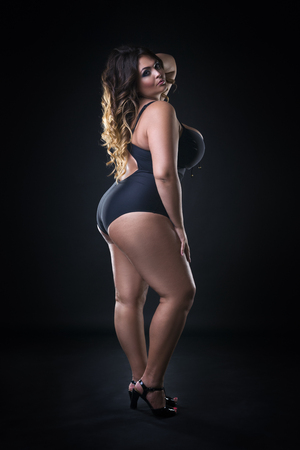Young beautiful caucasian plus size model in swimsuit, xxl woman on black background, full length portraitの写真素材