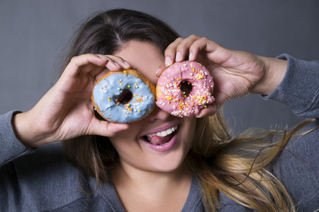 Happy beautiful young caucasian plus size model posing with donuts on a gray studio background, fast food and unhealthy nutrition conceptの写真素材