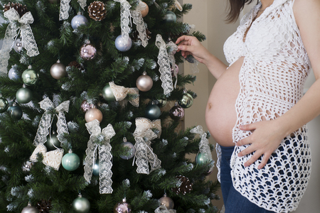 Young pregnant woman posing on the background of Christmas tree, holiday concertの写真素材