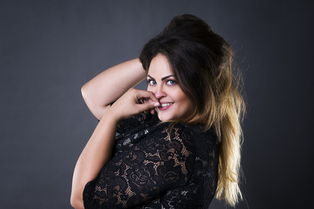 Young beautiful plus size model in black lace dres, xxl woman portrait on gray studio background, makeup and hairstyleの写真素材