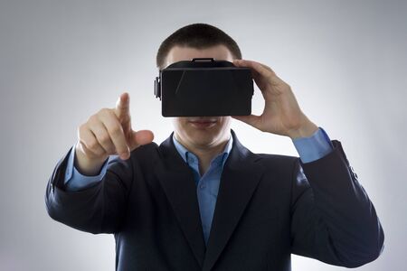 Young businessman uses a virtual reality glasses on gray backgroundの写真素材