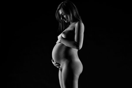 Beautiful naked pregnant woman on black studio background, pregnancy nude concept, art black and white photographyの写真素材