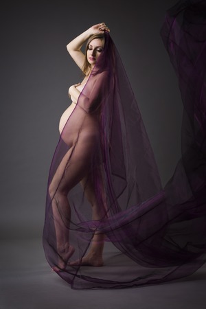 Beautiful naked pregnant woman with purple silk on gray background, pregnancy nude concept, art studio photographyの写真素材