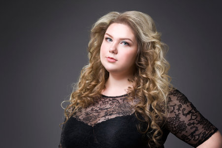 Young beautiful blonde plus size model in black dres, xxl woman portrait on gray studio background, makeup and hairstyleの写真素材