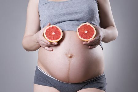 Pregnancy and nutrition - pregnant woman with fruits in hand on gray background, vegetarian diet, studio shotの写真素材