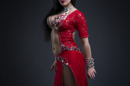Young beautiful exotic eastern women performs belly dance in ethnic red dress on gray background, studio shotの写真素材