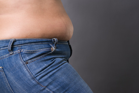 Woman with fat abdomen in blue jeans, overweight female stomach, stretch marks on belly closeup, gray studio backgroundの写真素材