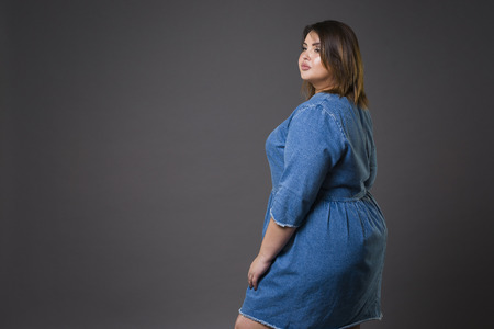 Plus size fashion model in casual jeans clothes, fat woman on gray studio background, overweight female body, full length portraitの写真素材