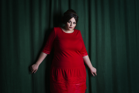 Plus size fashion model in red evening dress, fat woman on green background, professional make-up and hairstyleの写真素材