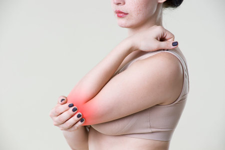Woman with pain in elbow, joint inflammation on beige backgroundの写真素材
