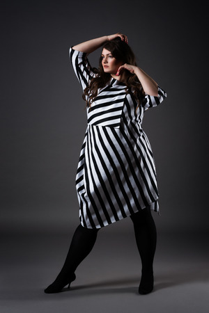 Plus size fashion model in striped dress, fat woman on gray studio background, overweight female body, full length portraitの写真素材