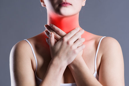 Sore throat, woman with pain in neck, gray background, studio shot