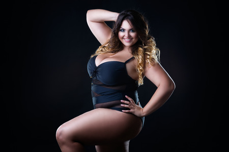 Happy plus size sexy model in swimsuit, fat woman with big natural breast on black studio background, overweight female bodyの写真素材