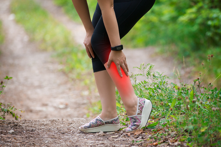 Pain in woman's shin, massage of female leg, injury while running, trauma during workout, outdoors conceptの写真素材