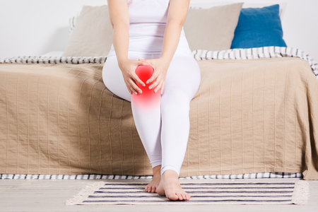 Woman with pain in knee suffering at home, painful area highlighted in redの写真素材