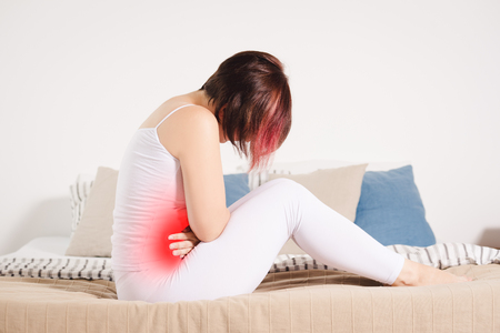 Stomach ache, woman with abdominal pain suffering at home, painful area highlighted in redの写真素材