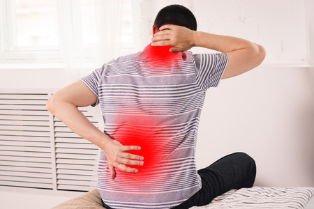 Neck pain, man suffering from backache at home, painful area highlighted in redの写真素材