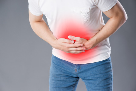 Man with abdominal pain, stomach ache on gray background, painful area highlighted in redの写真素材