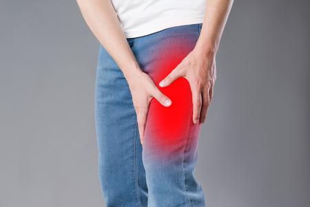 Man with pain in knee, studio shot on gray background, painful area highlighted in redの写真素材