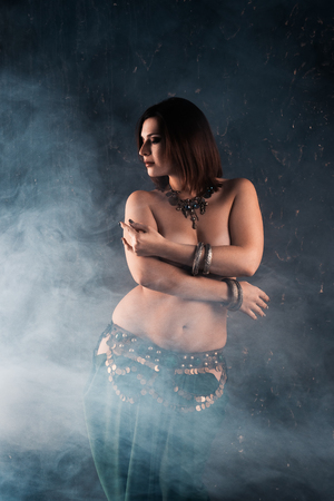 Sexy women performs belly dance in ethnic dress on dark smoky background, studio shotの写真素材