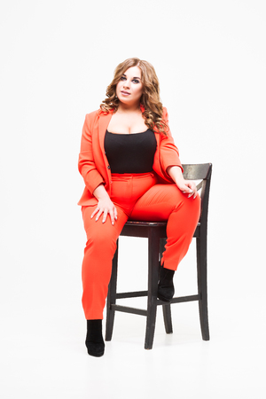 Plus size model with big breast and deep decollete, fat woman on white studio background in orange pantsuit, body positive conceptの写真素材