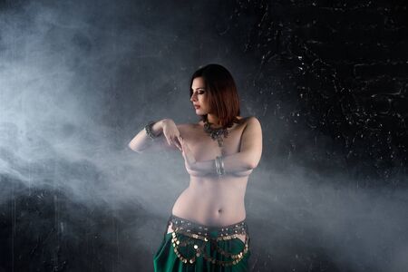 Sexy women performs belly dance in ethnic dress on dark smoky background, abstract art photography, studio shotの写真素材