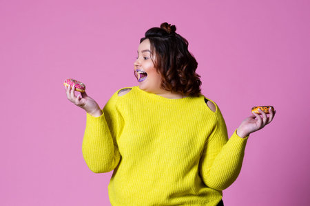 Cheerful plus size model with doughnuts, happy fat woman on pink background, unhealthy nutrition...
