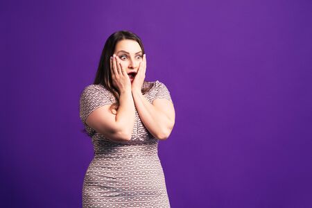 Shocked plus size model with wide open mouth on purple background, body positive conceptの写真素材