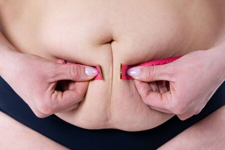 Fat woman with flabby belly measures waist size, overweight female body on gray background, diet conceptの写真素材