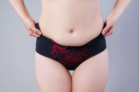 Woman in corrective panties, flabby belly after pregnancy, overweight female body on gray background, studio shotの写真素材