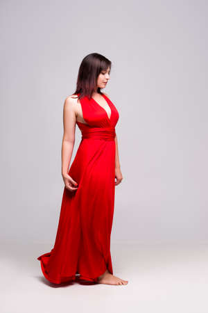 Beautiful woman in red dress in studio on gray background, full-length portraitの写真素材