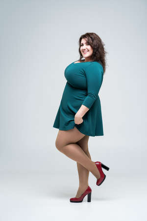 Happy plus size fashion model in green dress, fat woman on gray background, body positive concept, full length portraitの写真素材